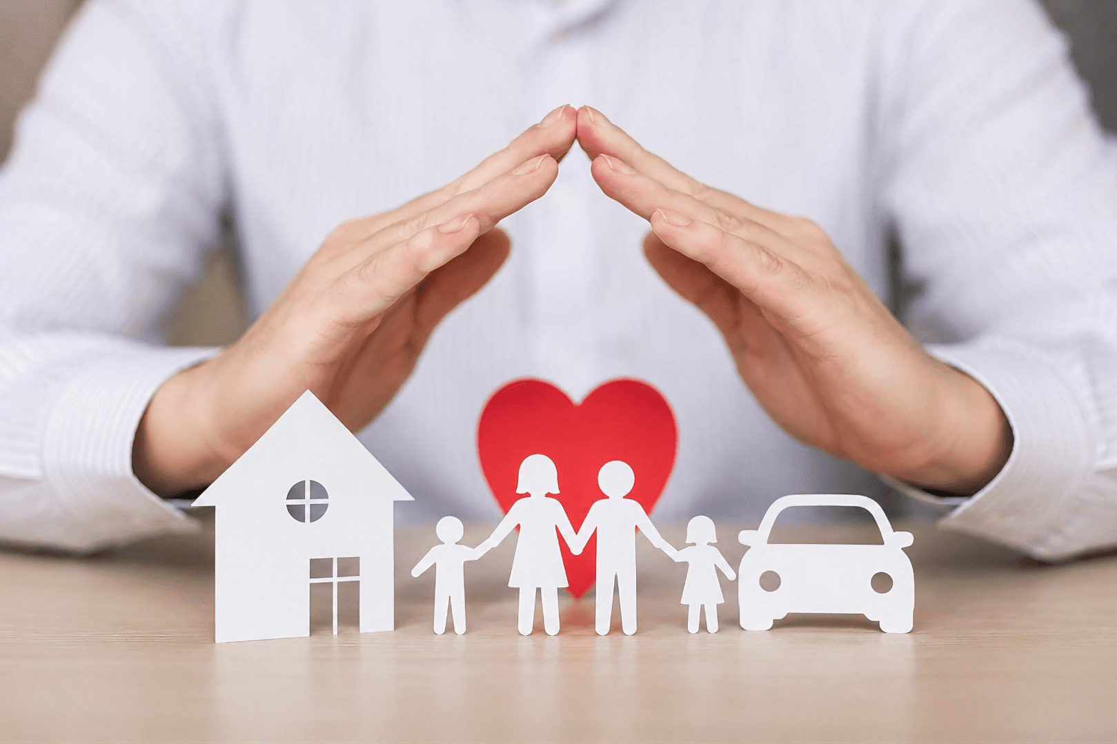 Hands sheltering paper cut-outs of a house, a family, a heart and a car