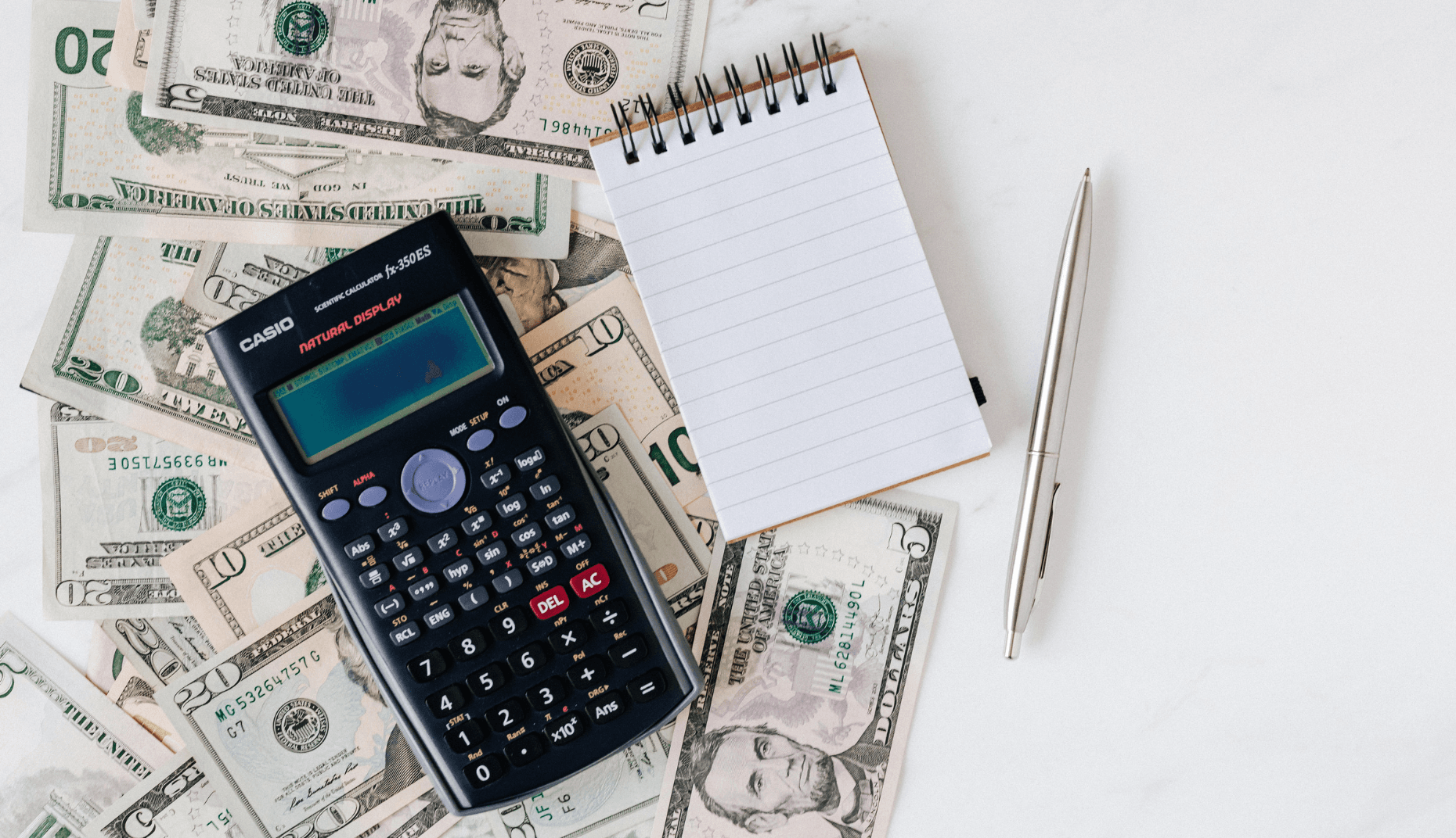 Calculator, banknotes, coins and a notepad laid out on a desk